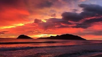 A beach with a sunset and mountains in the background.
