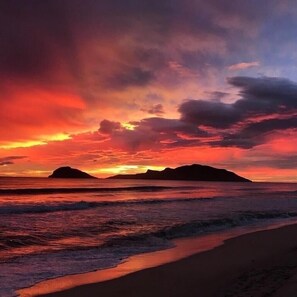 Ein Strand mit Sonnenuntergang und Bergen im Hintergrund.