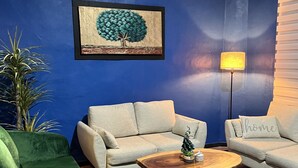 Un salon avec un mur bleu, deux canapés de couleur claire, un fauteuil vert, une table basse en bois, un petit sapin de Noël et une lampe.