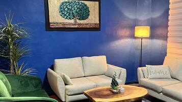 A living room with a blue wall, two light-colored sofas, a green armchair, a wooden coffee table, a small Christmas tree, and a lamp.