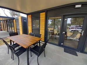 An outdoor dining area with a wooden table and black chairs, surrounded by a modern building with wooden paneling and large glass doors. - Sun and Sand Resort Mobile Home, Privlaka (Privlaka)