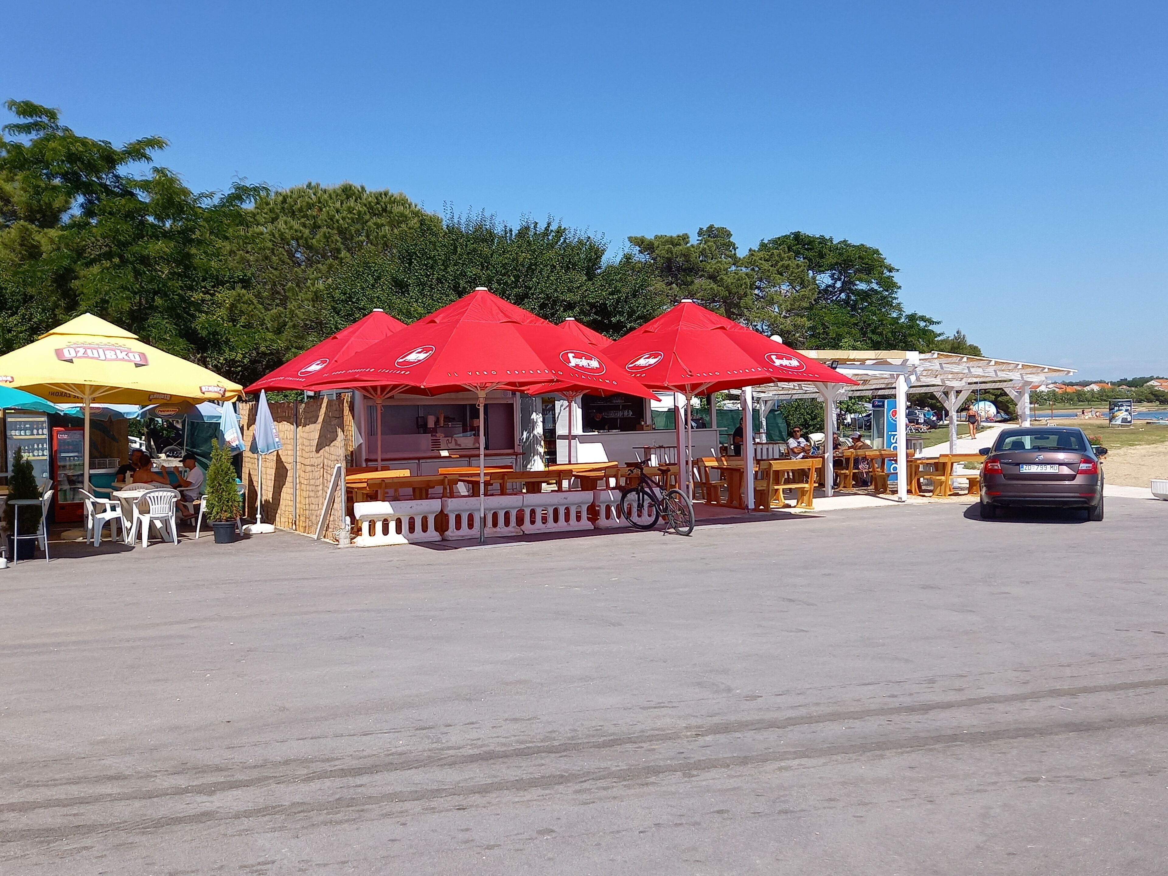 Outdoor food stalls with red umbrellas, wooden tables, and chairs.