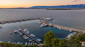 Un puerto deportivo con barcos amarrados, un muelle que se adentra en el agua y montañas al fondo.