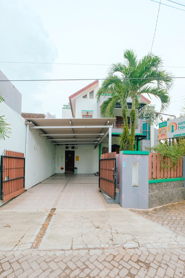 Un edificio residencial con entrada porticada, acceso mediante portón y una palmera.