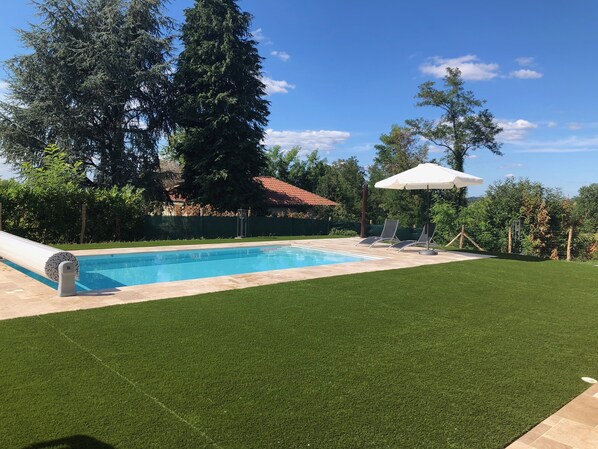 Una piscina con tobogán, rodeada de césped cuidado y árboles.