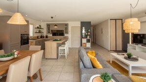 A modern kitchen with a central island, dining area with a wooden table and chairs, and a living area with a sofa and coffee table.