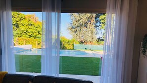 A living room with a large window, a sofa, and a view of a swimming pool and greenery.