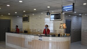 A reception desk with two staff members, a framed picture, a digital screen, and a distance marker sign. - Pearl City Hotel (Peshawar)