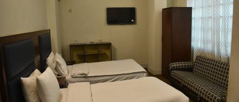 A hotel room with two beds, a TV, a sofa, and an air conditioning unit.