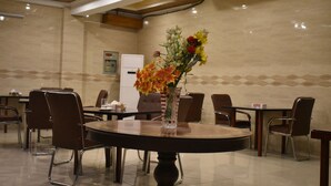 A dining area with a round table, chairs, and a vase with flowers. - Pearl City Hotel (Peshawar)