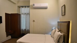 A hotel room with a bed, a bedside table with a phone and remote, an air conditioner, a door, and a curtain. - Pearl City Hotel (Peshawar)
