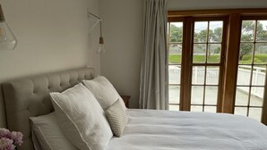 A bedroom with a large bed, white bedding, a potted plant, and a view of a deck through a window. - A private and spacious character home in Khandallah (Wellington)