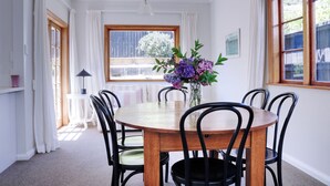 A dining room with a round wooden table, black chairs, and a vase of flowers. - A private and spacious character home in Khandallah (Wellington)