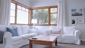 A living room with two white sofas, a wooden coffee table, and a lamp. - A private and spacious character home in Khandallah (Wellington)