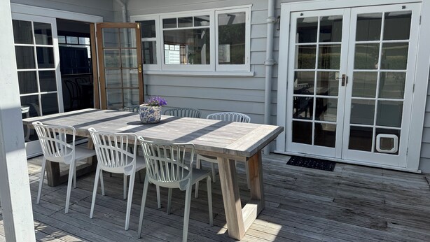 A covered patio with a wooden table and white chairs, a potted plant, and a sliding glass door. - A private and spacious character home in Khandallah (Wellington)
