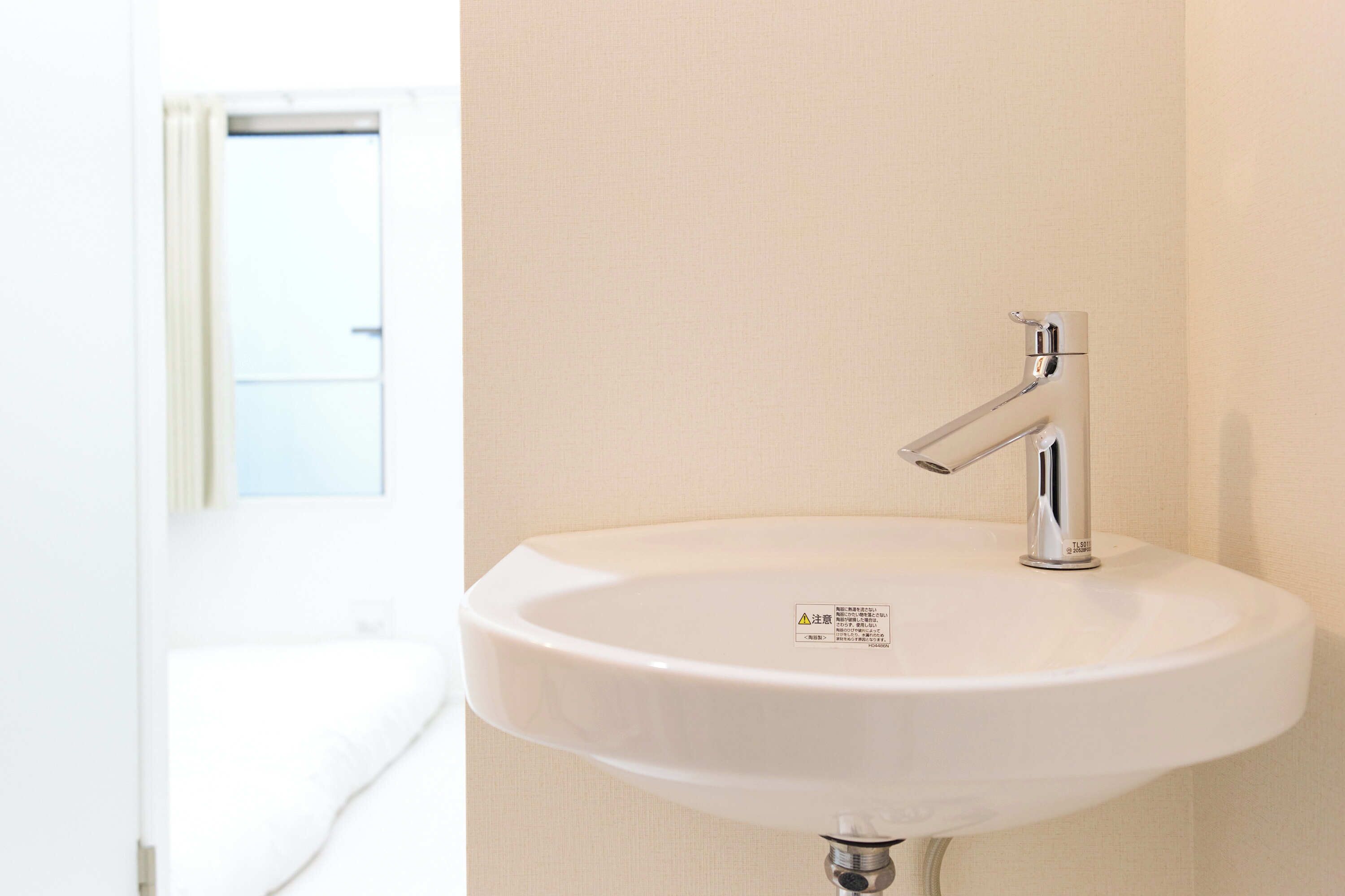 Een witte wastafel met een chromen kraan, bevestigd aan een beige muur.
