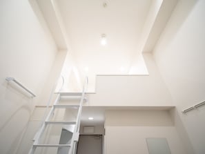 A narrow, white-walled room with a skylight, a white ladder, and a small door. - Studio G2 (Tokyo)