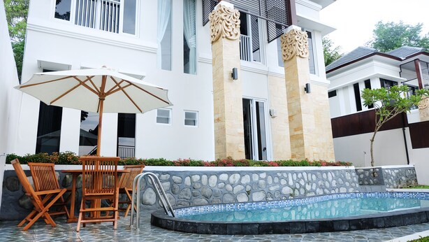 A modern house with a swimming pool, outdoor furniture, and decorative stone walls. - Villa Jogja Grand Bale with Private Pool by Simply Homy (Bangunjiwo)