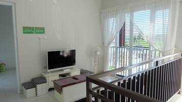A room with a TV on a white stand, a standing fan, and a small table with a colorful cloth. There are two signs on the wall, one indicating a no-smoking area and the other a no-smoking zone.
