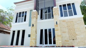 A multi-story building with a white facade, large windows, and decorative stone accents. - Villa Jogja Grand Bale with Private Pool by Simply Homy (Bangunjiwo)
