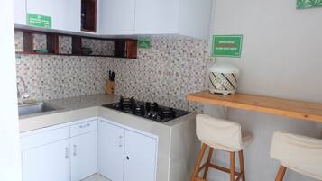 A kitchen with a tiled backsplash, a gas stove, a sink, and a wooden shelf with a rice cooker.
