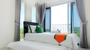 A double bed with white bedding and green and orange accents, a black headboard, and a view of greenery through large windows. - Villa Jogja Grand Bale with Private Pool by Simply Homy (Bangunjiwo)
