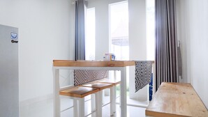 A room with a wooden table, a bench, and a window with curtains. - Villa Jogja Grand Bale with Private Pool by Simply Homy (Bangunjiwo)