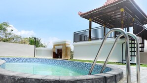 A swimming pool with a metal ladder, a covered patio, and a stone wall. - Villa Jogja Grand Bale with Private Pool by Simply Homy (Bangunjiwo)
