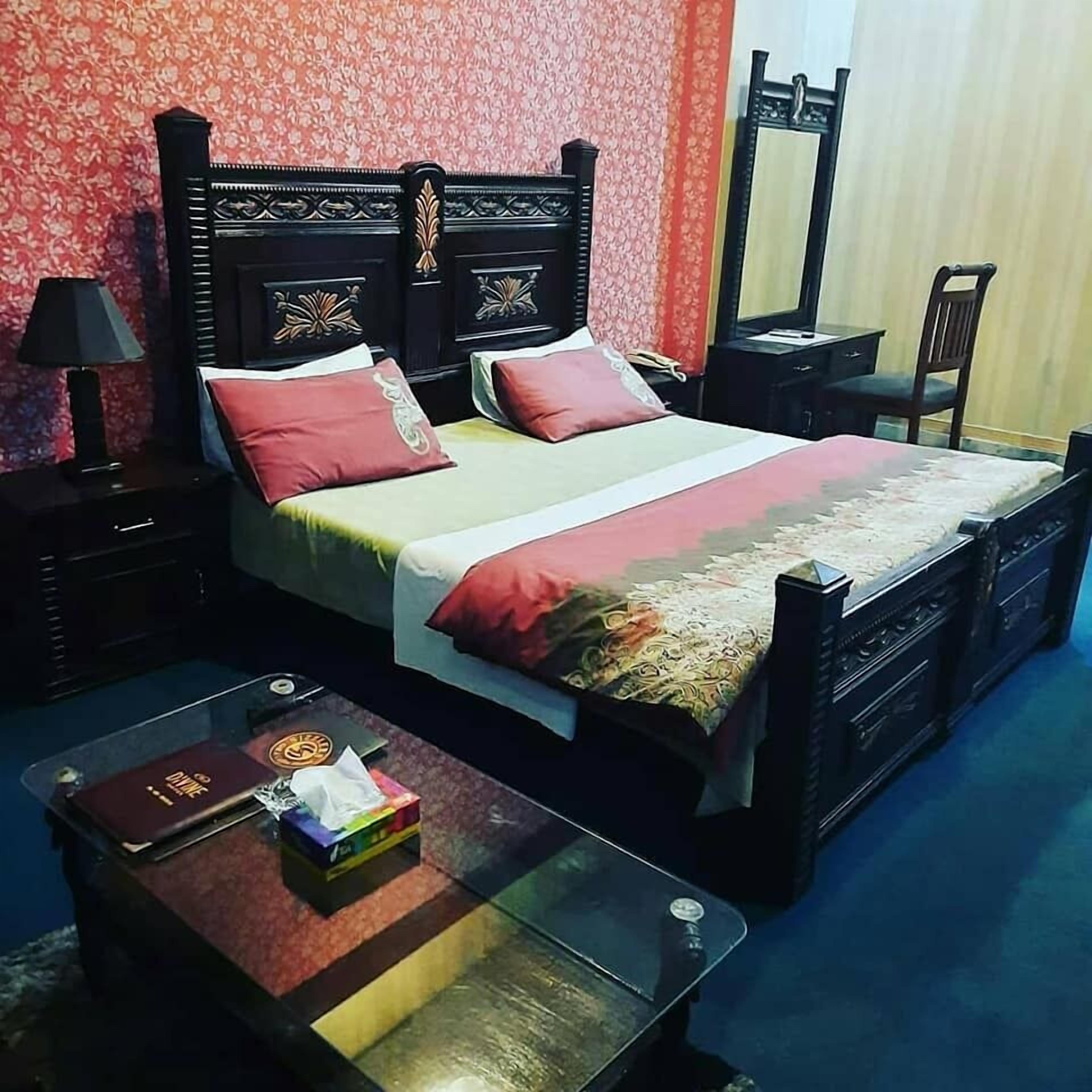Cama bem arrumada com cabeceira, mesa de cabeceira com abajur e pequena mesa com um livro e lenços.
