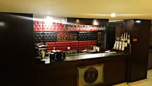 Eine Barbereich mit einer rot und schwarz gepolsterten Wand, einer Glastheke und einem Schild mit der Aufschrift 'Sizzlers'.