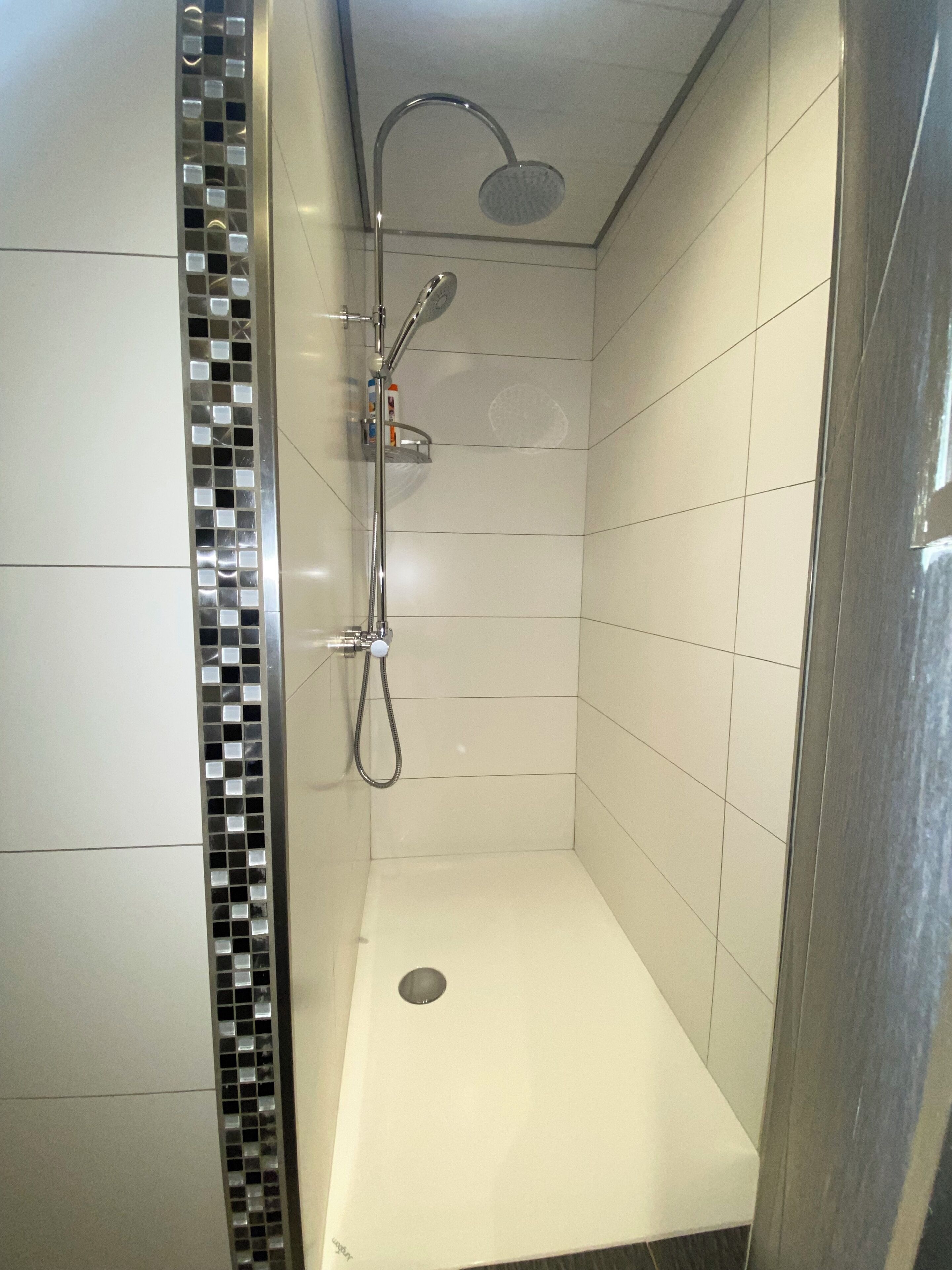 Een kleine, betegelde douchecabine met een chromen douchekop en een handdouche.