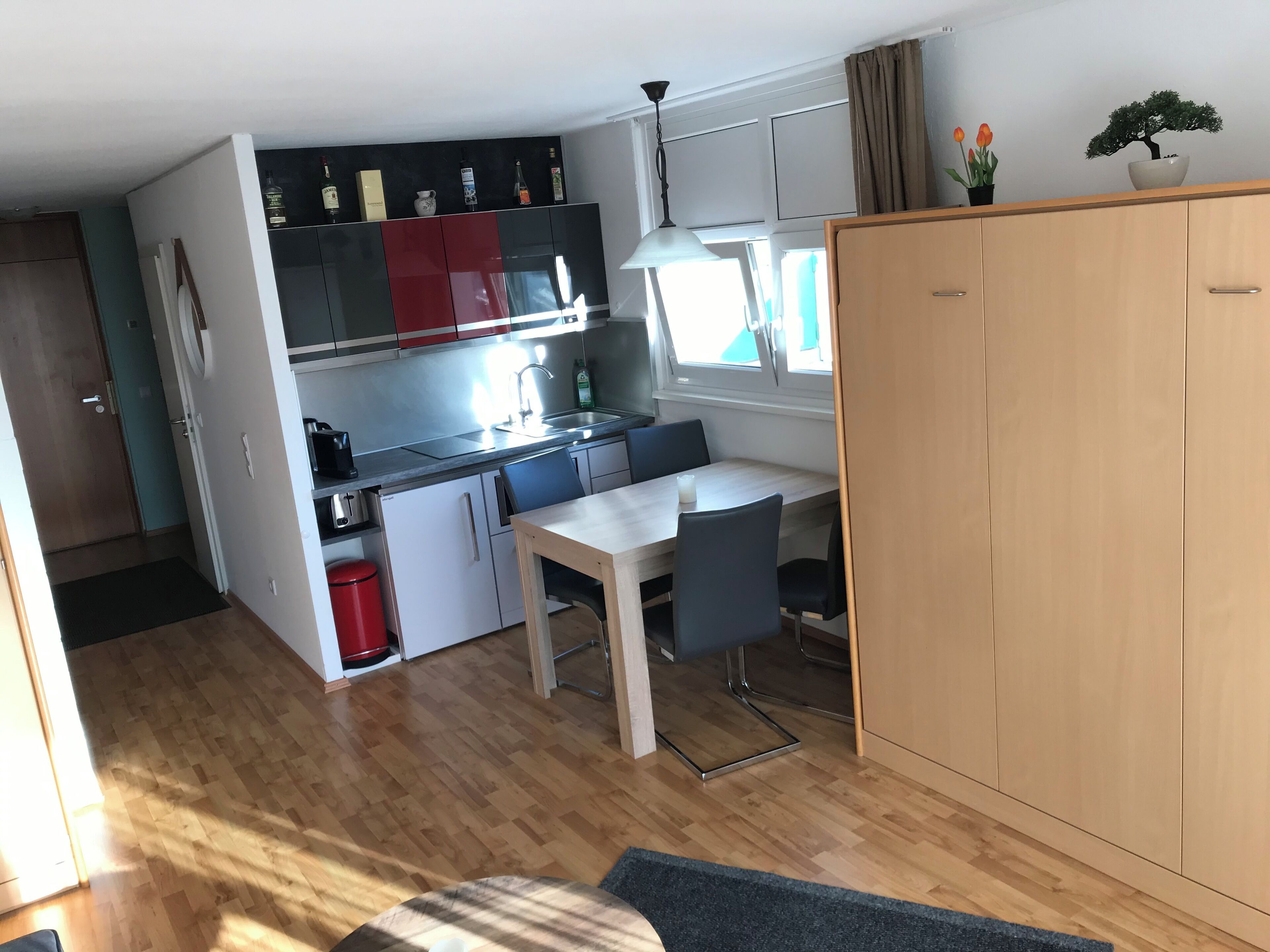 Eine kompakte Küche mit Essbereich, einem Holzschrank und einem Fenster mit Vorhängen.
