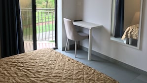 Une chambre d’hôtel équipée d’un lit, d’un bureau, d’une chaise, d’une télévision et d’un balcon donnant sur un paysage verdoyant.