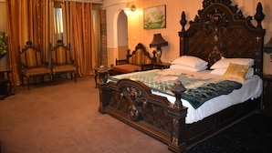 A traditional bedroom with a large ornate bed, a sitting area with chairs, and a painting on the wall. - Undrah Inn Hotel (New Mirpur City)