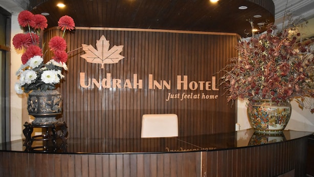 A reception desk at Undrah Inn Hotel with a wooden panel design, a maple leaf logo, and a vase with flowers. - Undrah Inn Hotel (New Mirpur City)