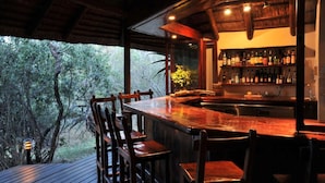 Zona de bar con mostrador de madera, sillas y vista a árboles a través de amplias ventanas.