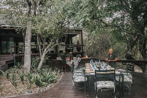 An outdoor dining area with tables and chairs, surrounded by trees and a wooden deck. - Waterbuck Lodge (Hoedspruit)