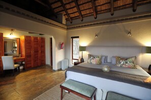 A bedroom with a large bed, a nightstand, a mirror, a desk, and a wardrobe. - Waterbuck Lodge (Hoedspruit)