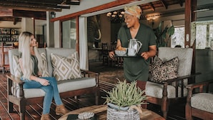 Un ambiente interior acogedor con muebles de madera, una zona de bar al fondo y una persona sirviendo café.