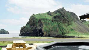 A wooden picnic table and a hot tub in front of a rocky cliff by the sea. - Luxury Ocean Villas (Vestmannaeyjar)