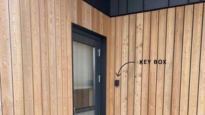 A room with wooden panel walls, a glass door, and a key box mounted on the wall. - Luxury Ocean Villas (Vestmannaeyjar)