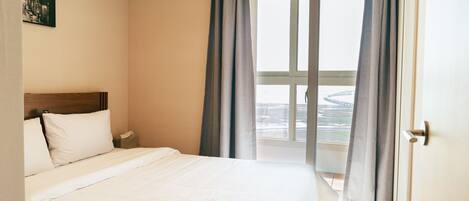 A hotel room with a bed, a nightstand, a window with curtains, and a view of a bridge.
