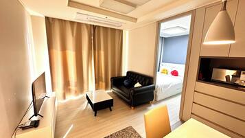 Una habitación de hotel moderna con una televisión de pantalla plana, un escritorio con una computadora portátil, un sofá de cuero negro, una mesita pequeña y una cama con cabecera blanca.