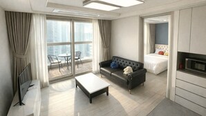 A modern hotel room with a sofa, a small table, a bed, and a view of the city through large windows.