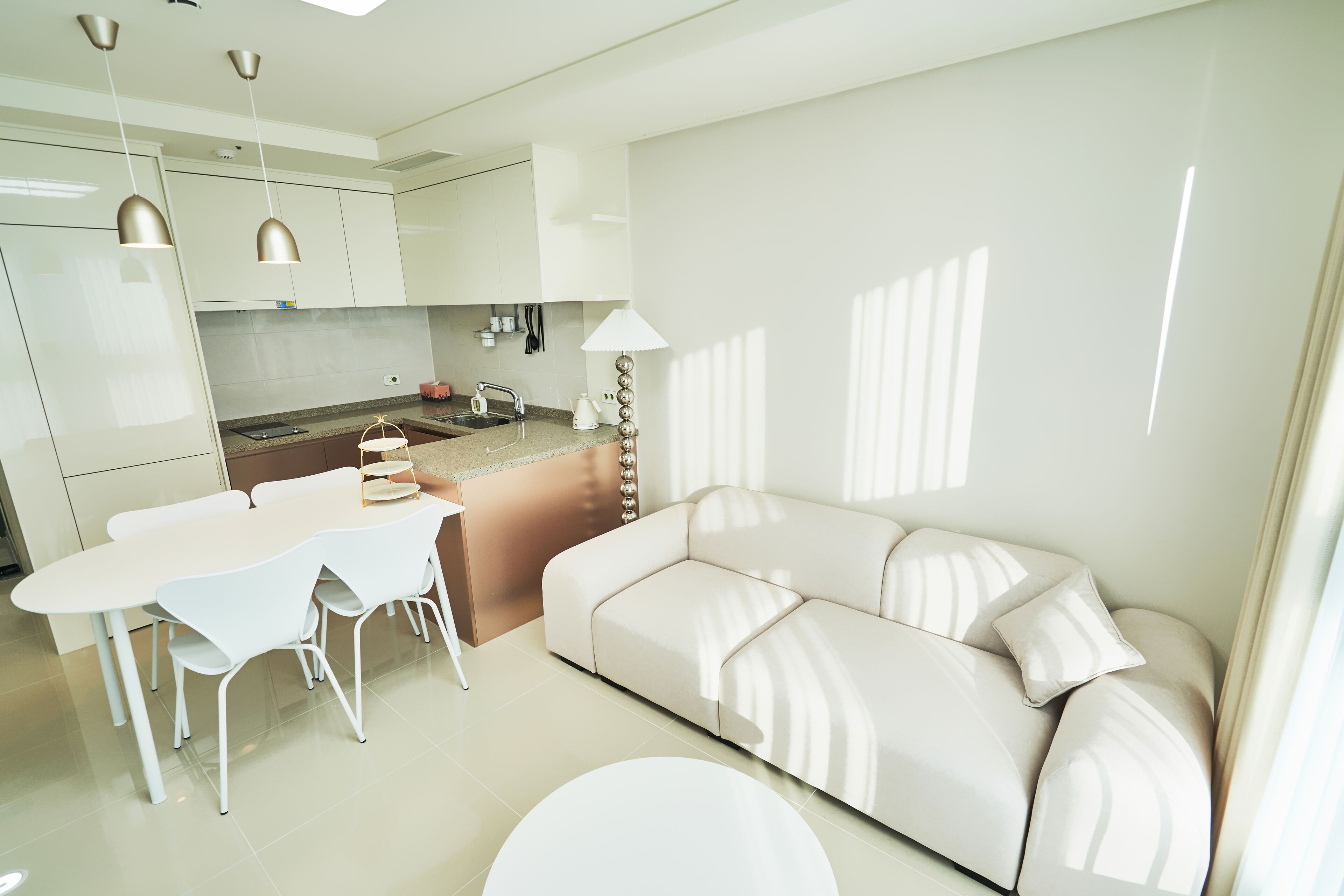 Une cuisine moderne avec des meubles blancs, une table à manger avec des chaises et un canapé beige.