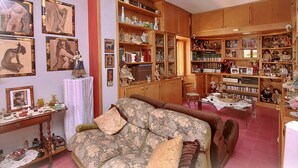 Een gezellige kamer met een bank, een tafel met decoratieve voorwerpen, en planken vol boeken en beeldjes.