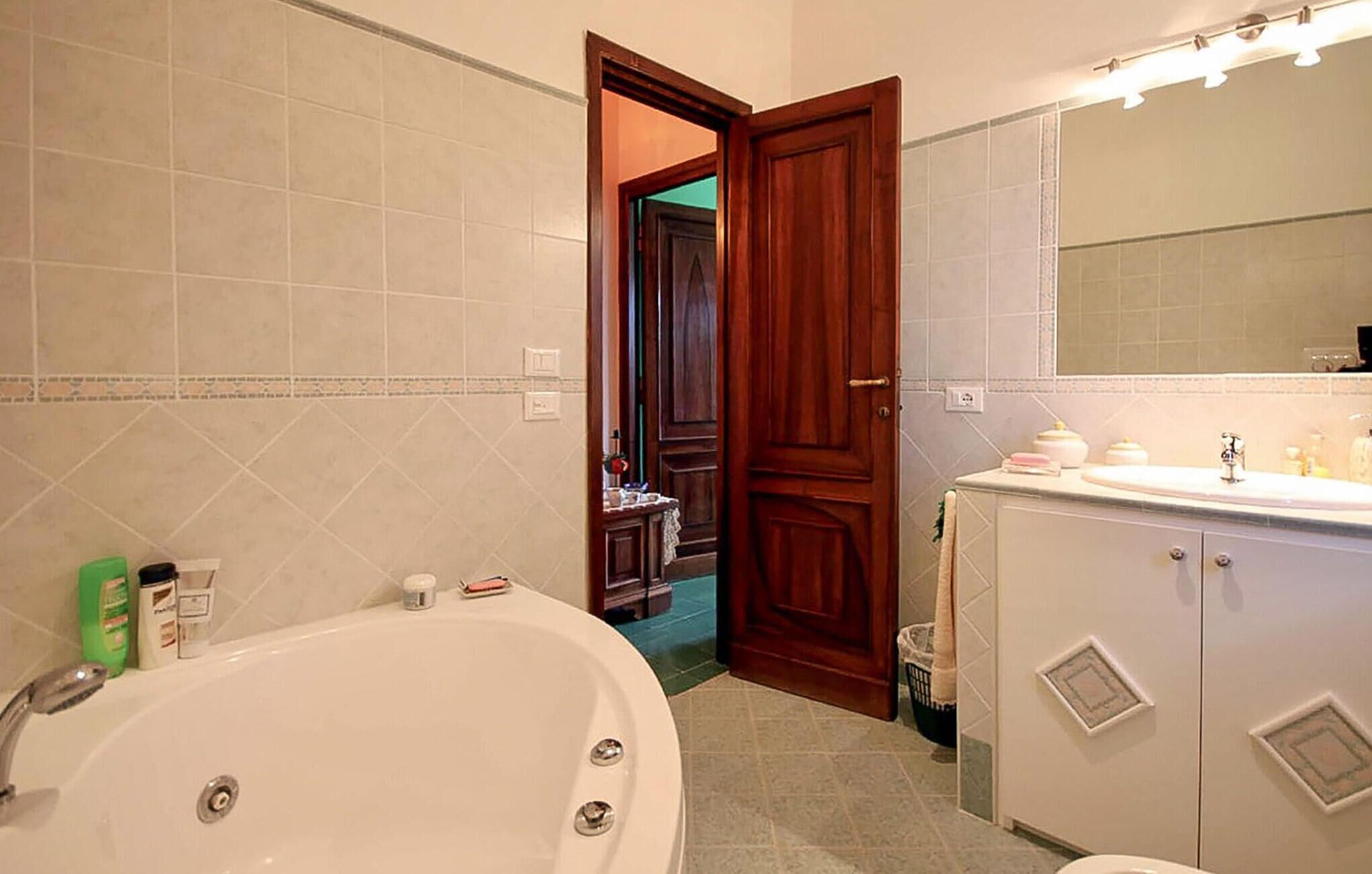 Un baño con bañera, lavabo con espejo y puerta que da a otra habitación.