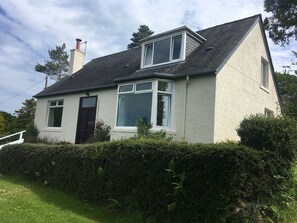 Charming two-story house with a pitched roof and chimney, surrounded by a well-manicured lawn and hedge.