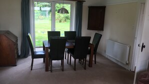 A dining area with a table and chairs, a radiator, and a view of the outdoors. - Detached house with stunning garden in picturesque coastal village SW Scotland (Kippford)