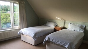 A bedroom with two single beds, a window with curtains, a radiator, and a bedside lamp. - Detached house with stunning garden in picturesque coastal village SW Scotland (Kippford)